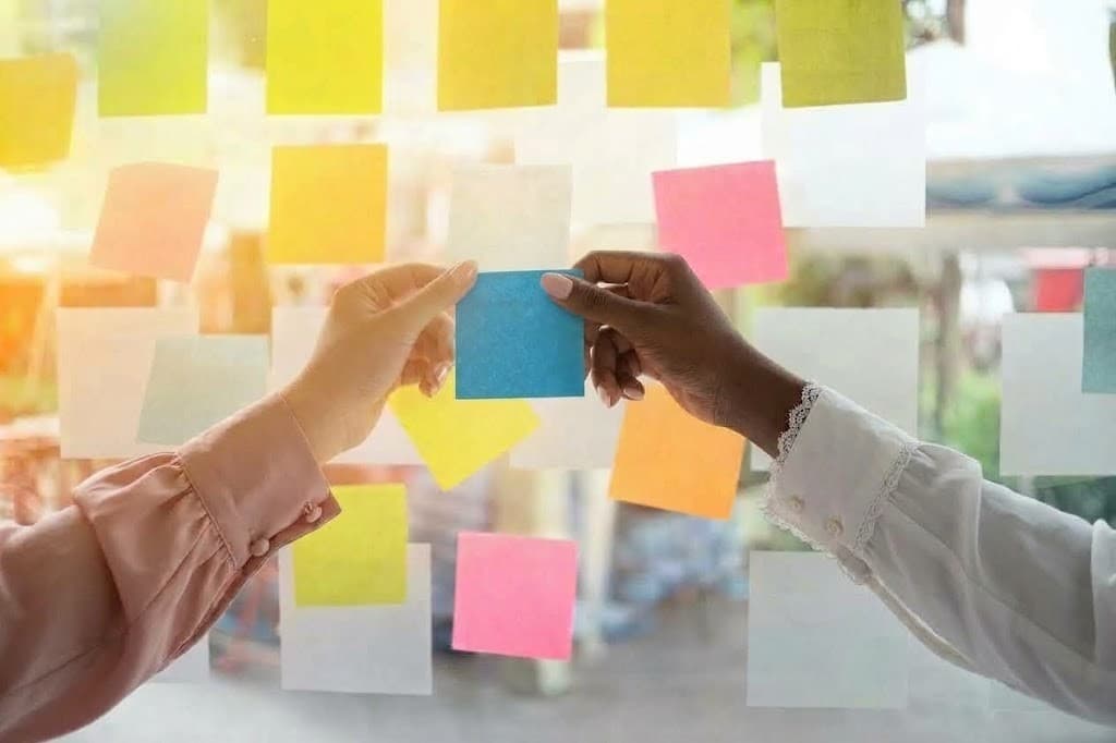 Two people placing a sticky note together on a glass wall